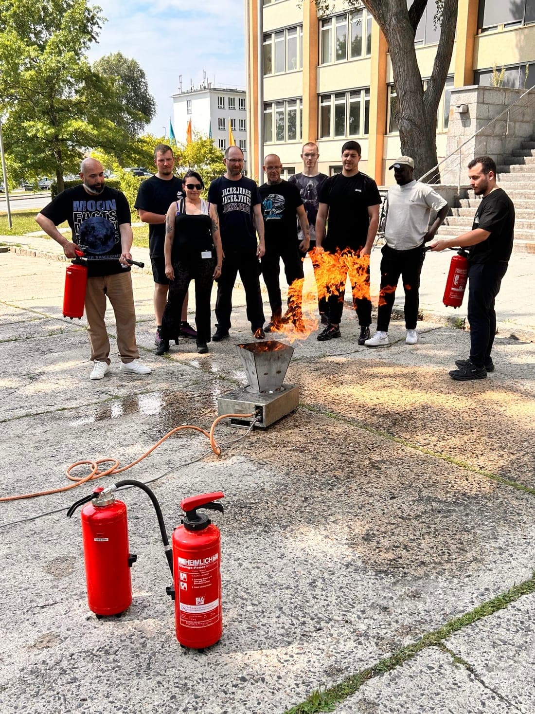 Teilnehmende einer Brandschutzhelfer-Ausbildung stehen mit Feuerlöschern um die brennende Gassimulationsanlage