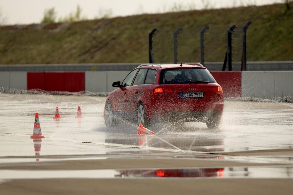 Kombi mit hoher Gischt bei der Aquaplaning-Übung auf der Wasserfläche