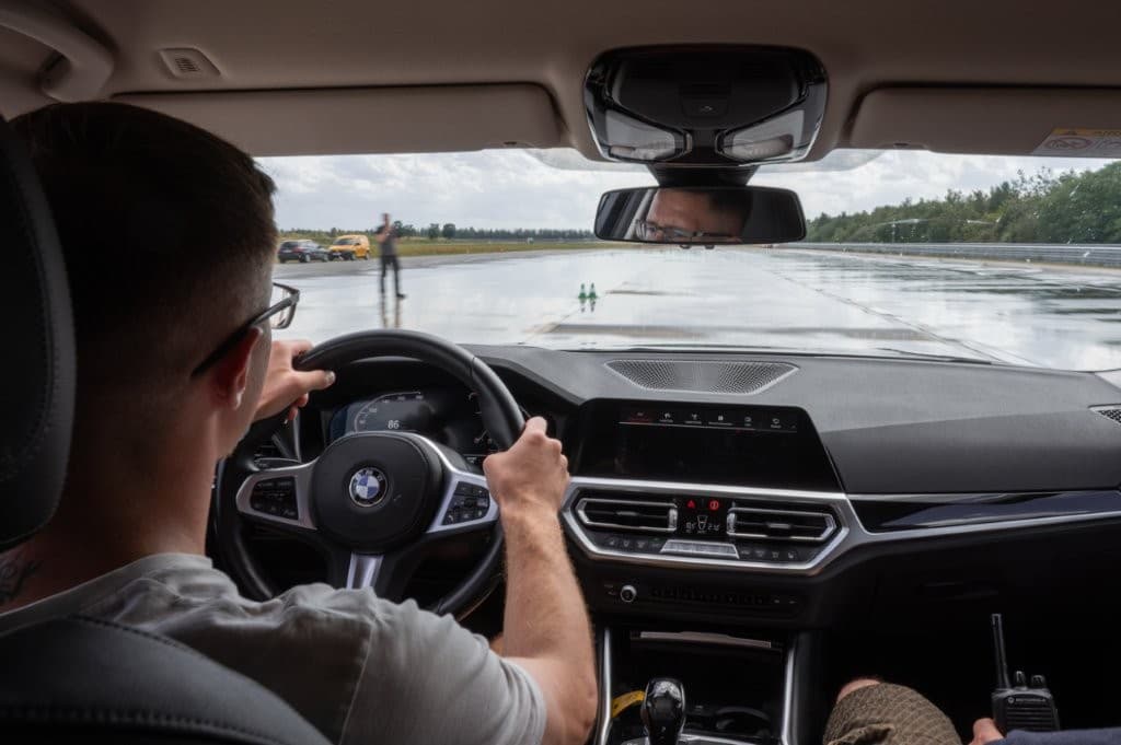 Blick aus dem Fahrzeuginneren auf die nasse Übungsstrecke, der Trainer sitzt mit Funkgerät auf dem Beifahrersitz