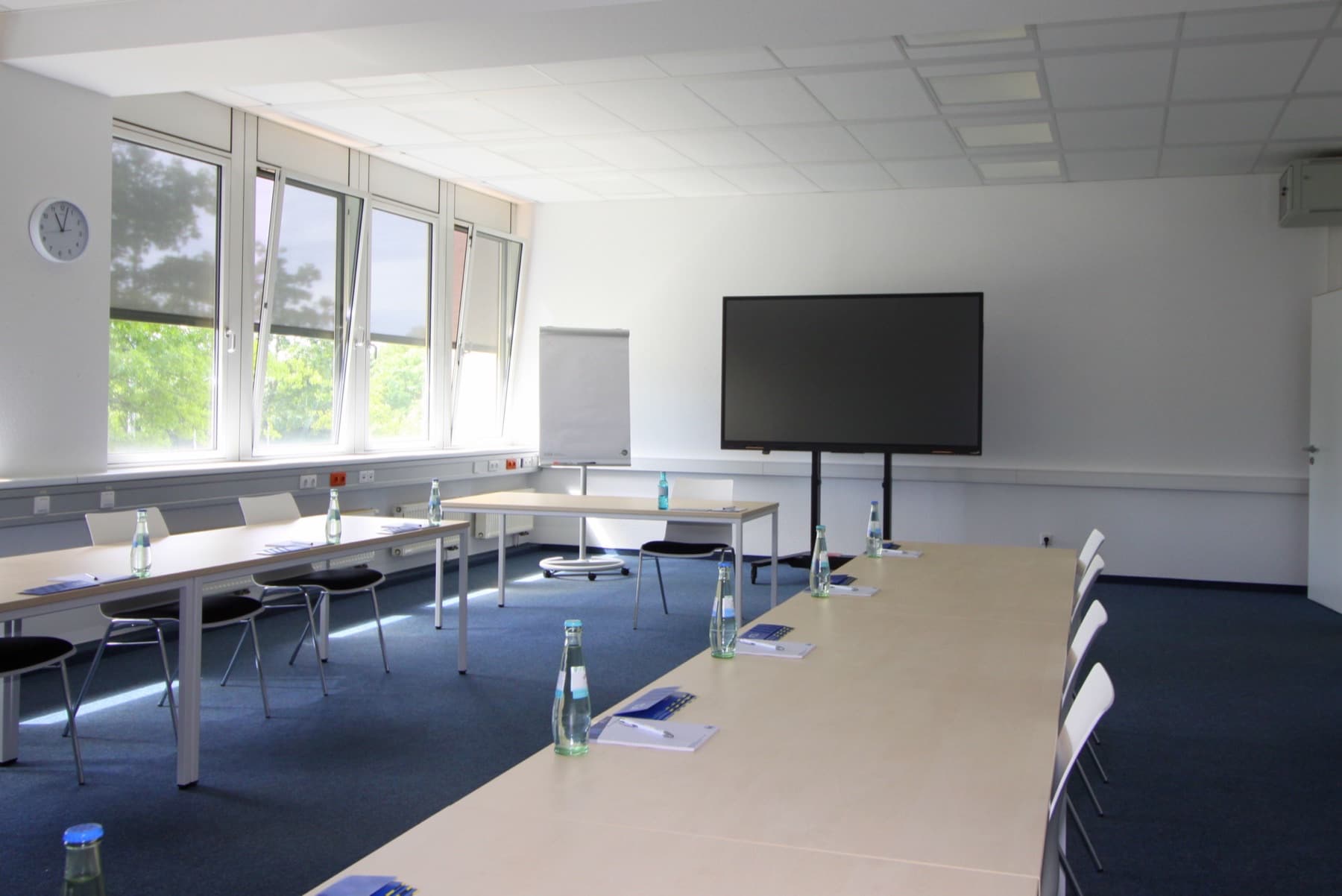 Seminarraum mit langer Tafel, Präsentationsbildschirm und Flipchart
